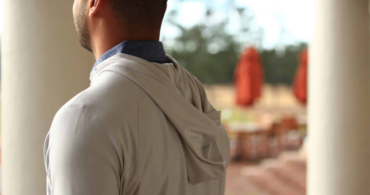 A man stands with his back to the camera, wearing a light gray hoodie pullover