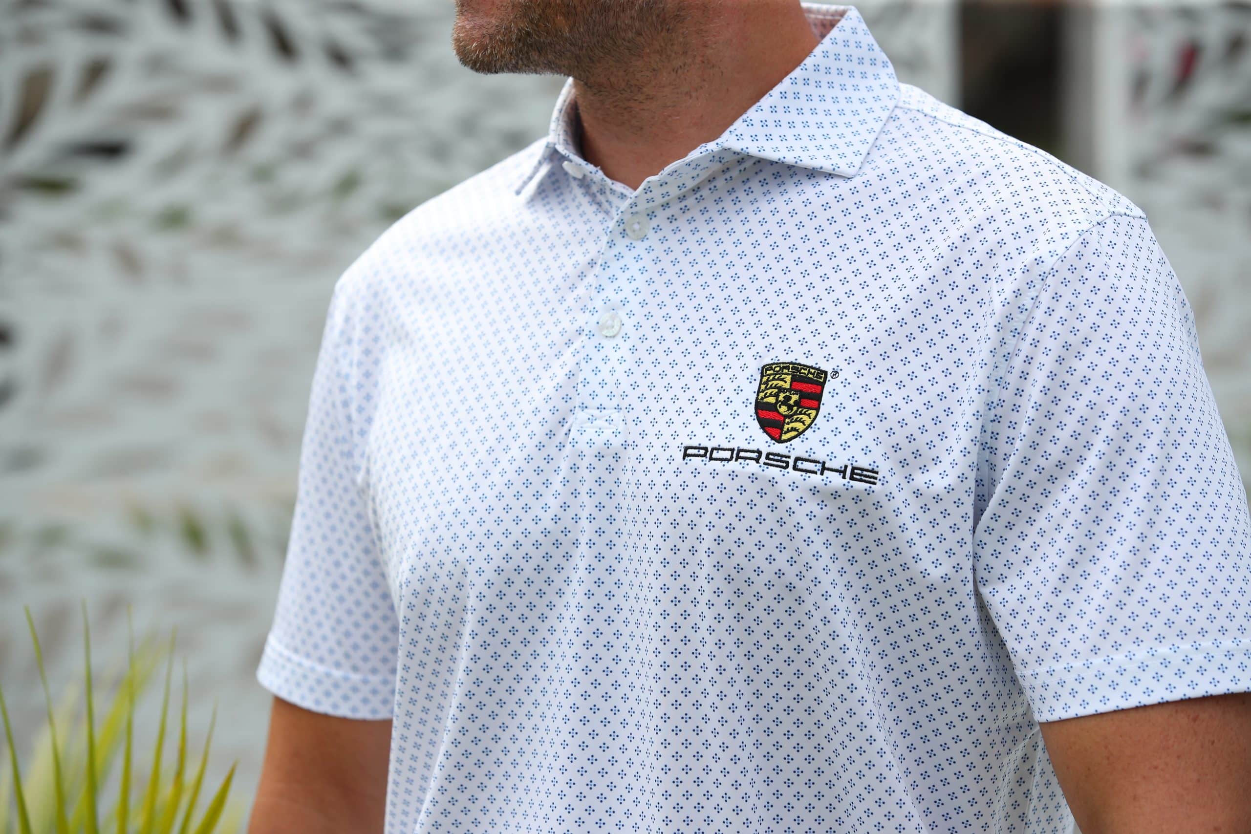 A person wearing a white polo shirt with a blue geometric pattern and a Porsche logo on the chest