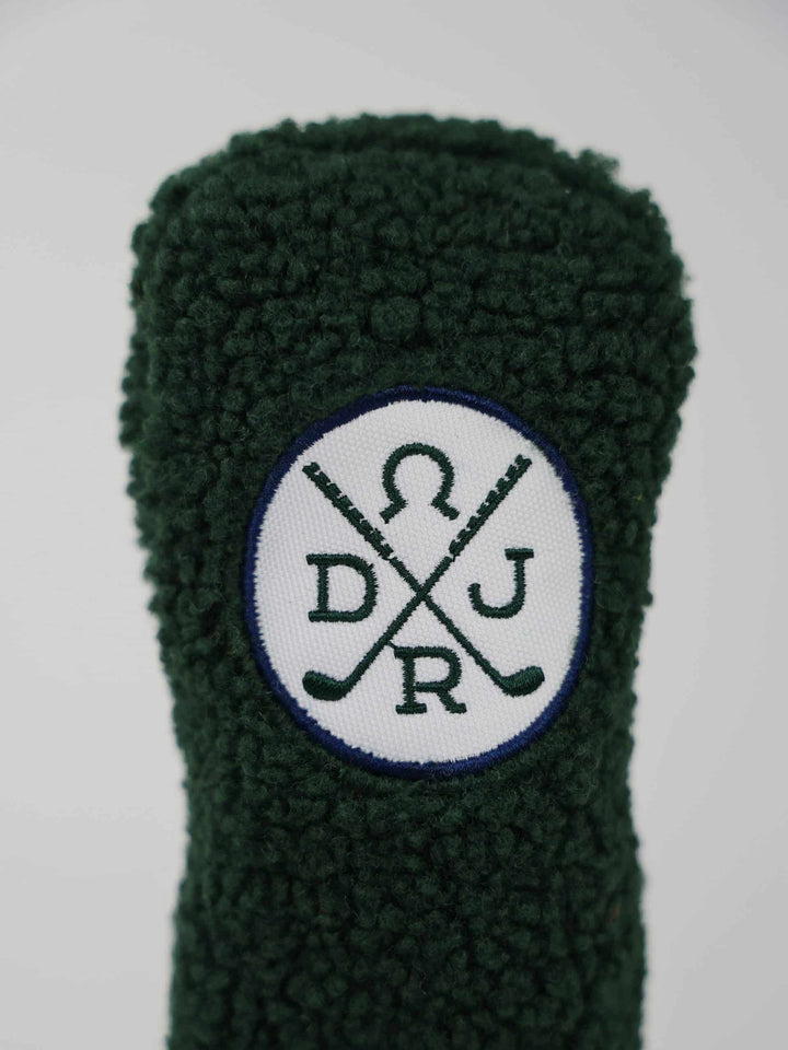 Close-up of a textured dark green fabric golf club head cover with a circular logo