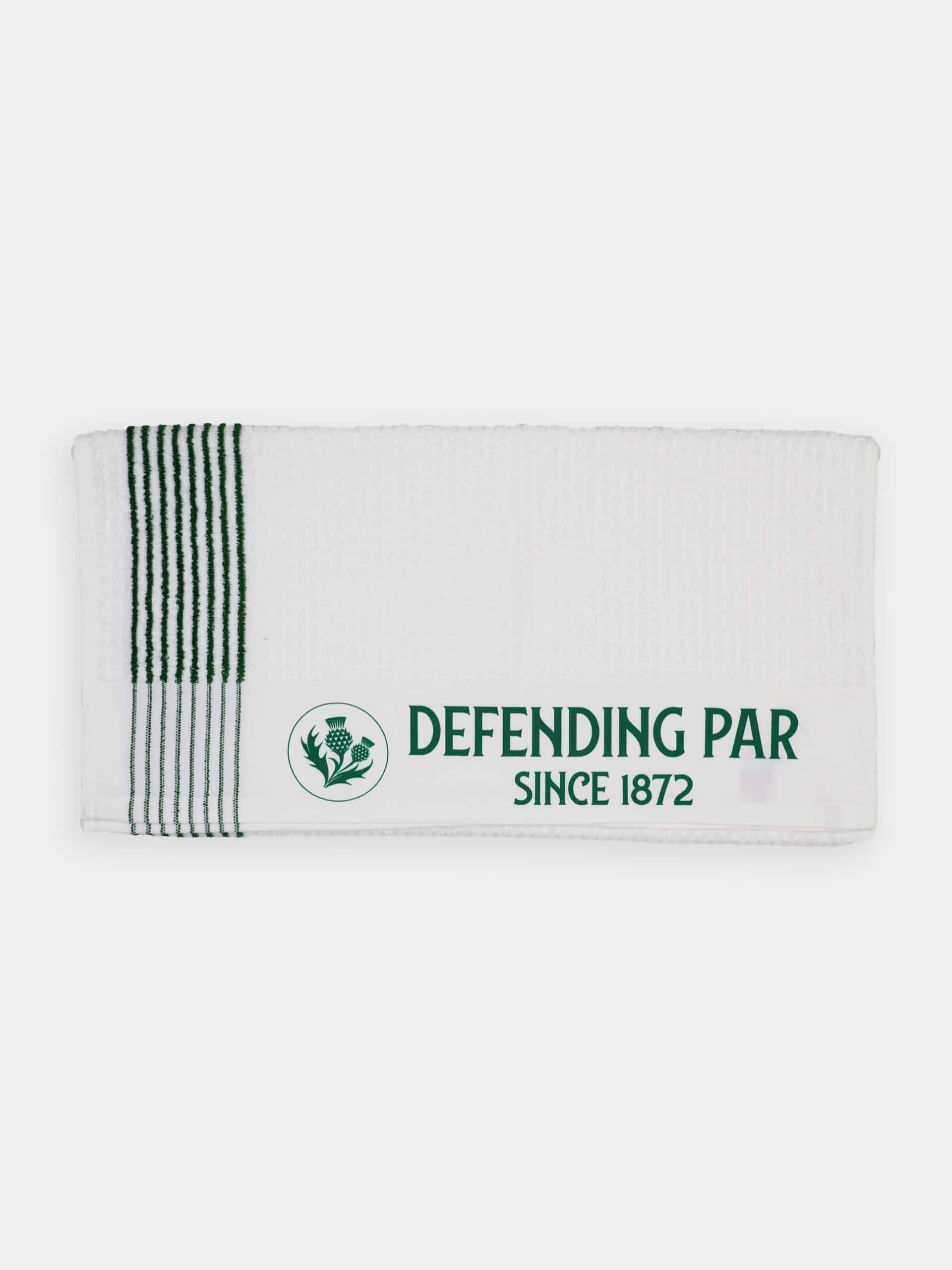 White towel with a green-striped edge displays a circular thistle emblem and the text "DEFENDING PAR SINCE 1872" in bold green font