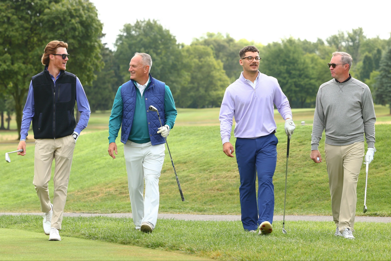 Four men walking on a foggy golf course wearing golf layers