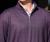 A person wearing a purple zip-up sweater with a subtle plaid pattern, layered over a light purple collared shirt, in bright daylight.