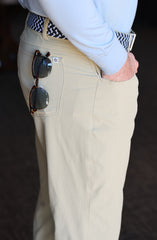 A person in beige pants with a patterned belt and light blue shirt has sunglasses hanging from the back pocket. The tone is casual and relaxed.