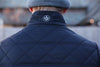 A person wearing a quilted black jacket with a floral patch under the collar and a gray beanie stands outdoors, conveying a casual, cool vibe.