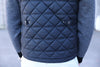 Close-up of a person wearing a quilted black vest with a diamond pattern and gray herringbone patterned sleeves. The tone is casual and modern.