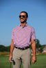 A man wearing a red and white striped polo shirt and khaki pants stands on a golf course holding a putter.