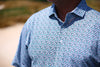 A man wears a light blue short-sleeved polo shirt with a subtle multicolored speckled pattern and a classic collar.