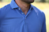 Man wearing a bright blue polo shirt with a patterned contrast placket, standing outdoors on a golf course.