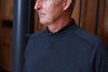 Middle-aged man wearing a dark navy textured crewneck sweater, photographed in profile against an interior backdrop.
