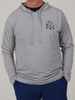 Man in a gray hooded sweatshirt with crossed golf club logo on chest, paired with blue pants. His hands are in pockets, conveying a relaxed vibe.