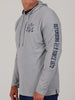 Man in a gray hooded sweatshirt with text on sleeve, "Defending Fair Since 1972," and crossed hockey sticks on chest. Casual, sporty vibe.