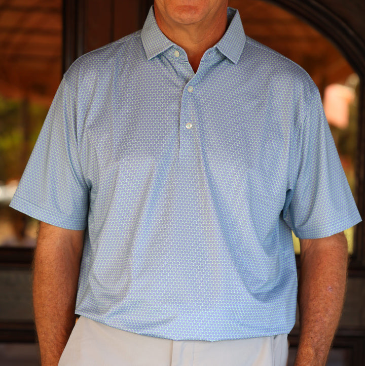 A man stands wearing a light blue patterned polo shirt with short sleeves.
