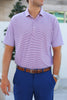 A man wearing a striped red and white polo shirt and blue pants stands with his hands at his sides.