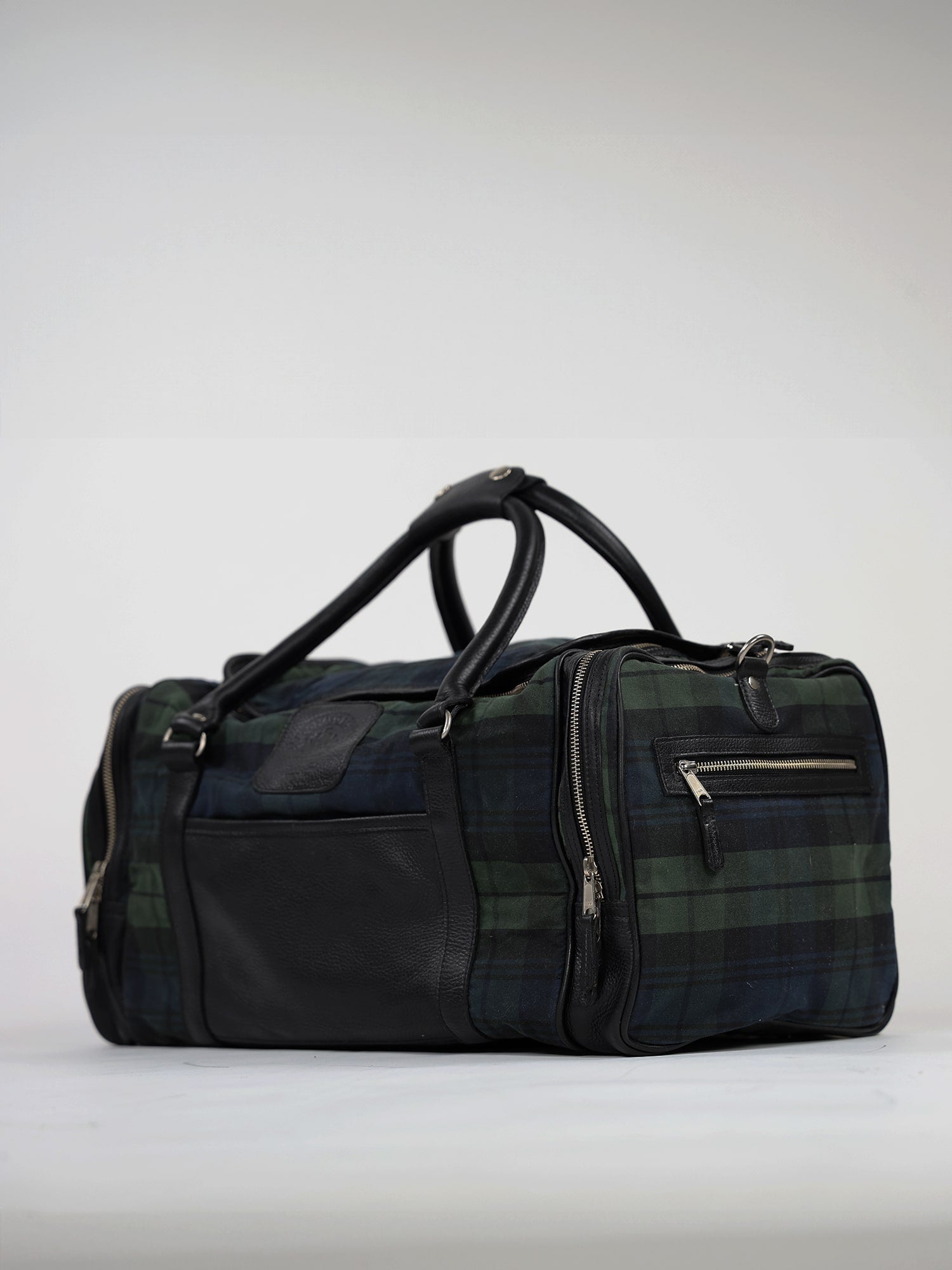 A stylish plaid duffel bag with black leather accents and multiple zippered compartments