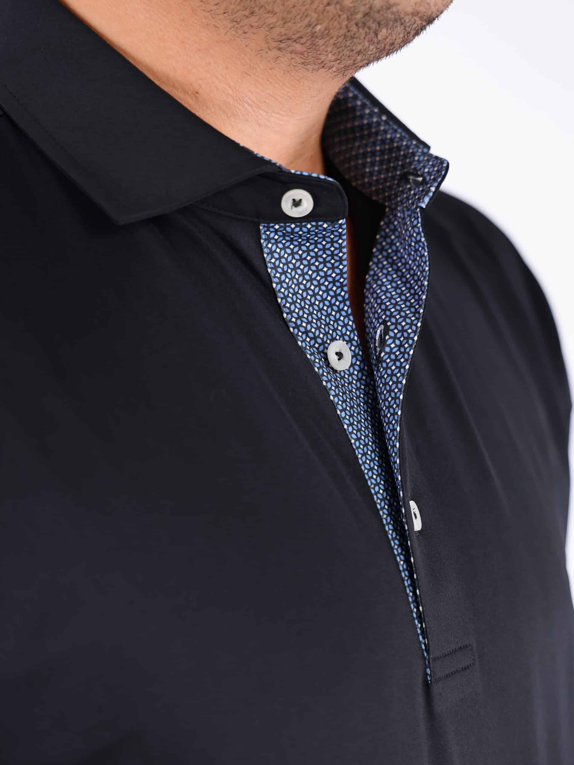 Close-up of a person wearing a black collared shirt with a blue patterned inner lining and white buttons