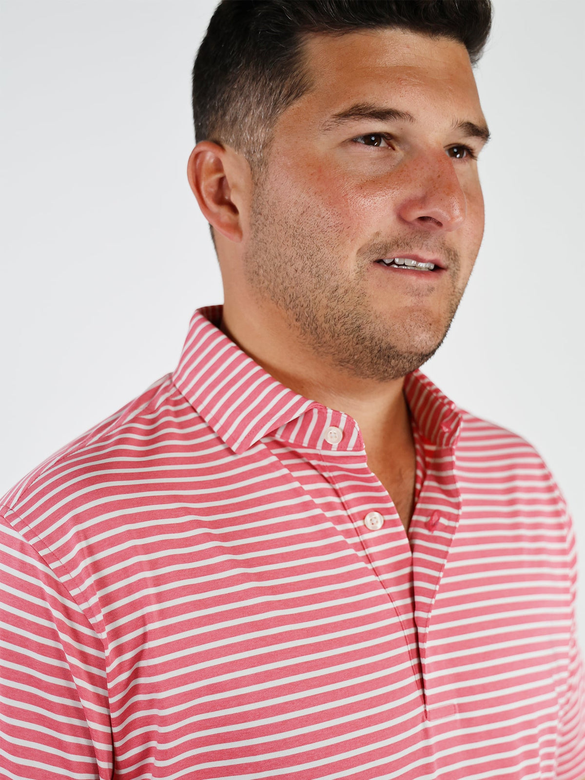 A person wearing a red and white striped polo shirt looks to the side with a slight smile. The background is plain white, giving a clean and bright feel.