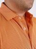Close-up of a man wearing an orange polo shirt with thin black stripes. The shirt features a buttoned collar and the image conveys a casual, relaxed vibe.