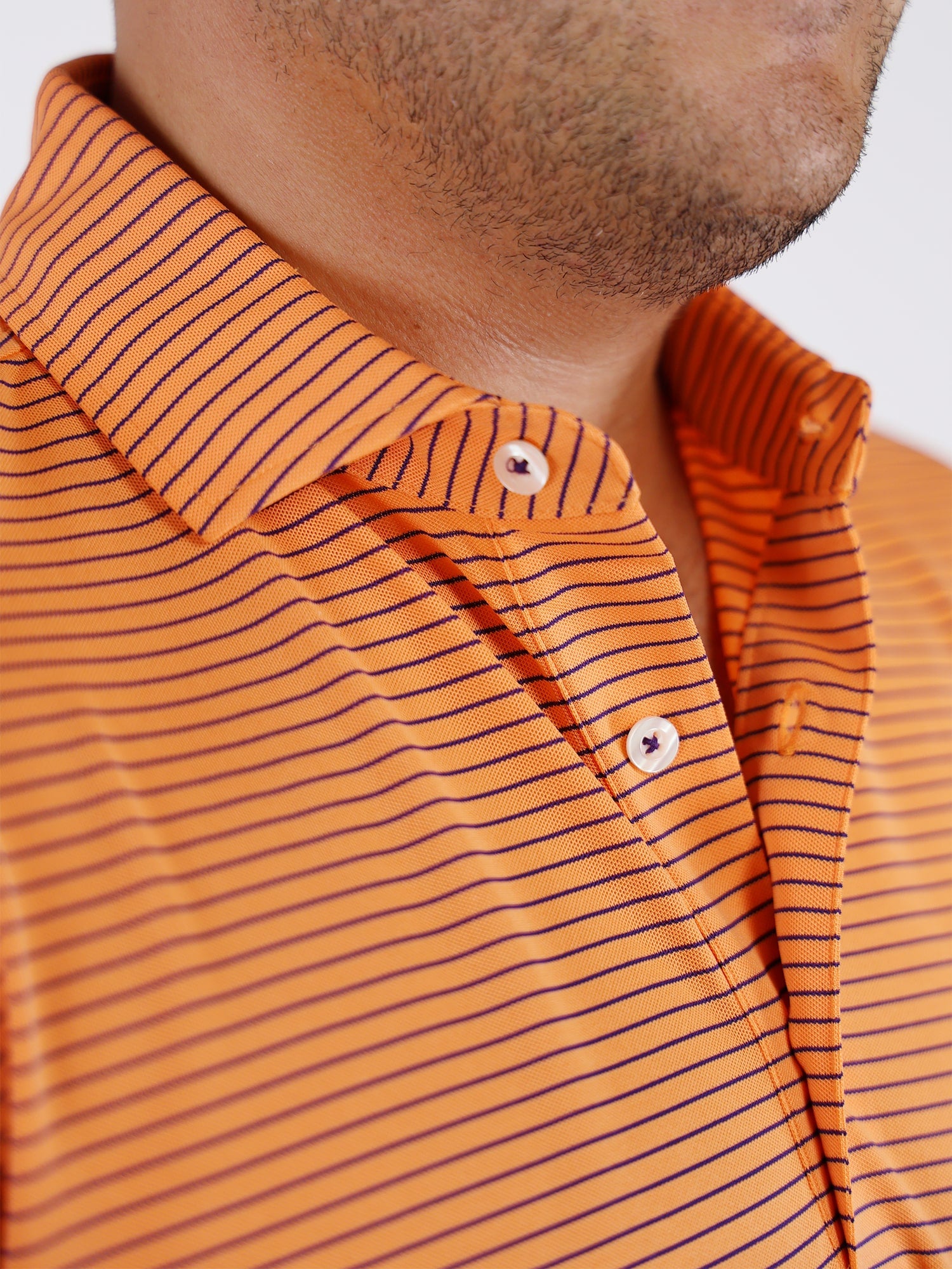Close-up of a man wearing an orange polo shirt with thin black stripes. The shirt features a buttoned collar and the image conveys a casual, relaxed vibe.