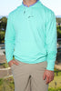 A person is standing with their hand on their hip, wearing a mint green hoodie over a collared shirt and light-colored pants.