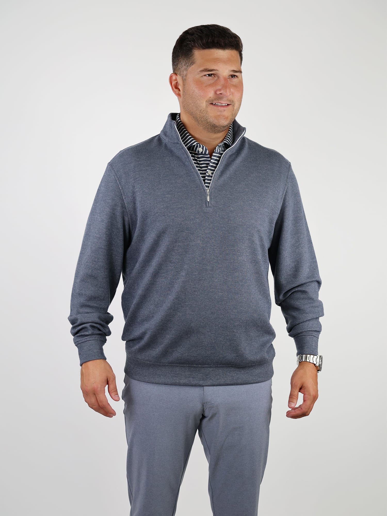 A man stands smiling in a light gray quarter-zip sweater over a striped shirt with matching pants.