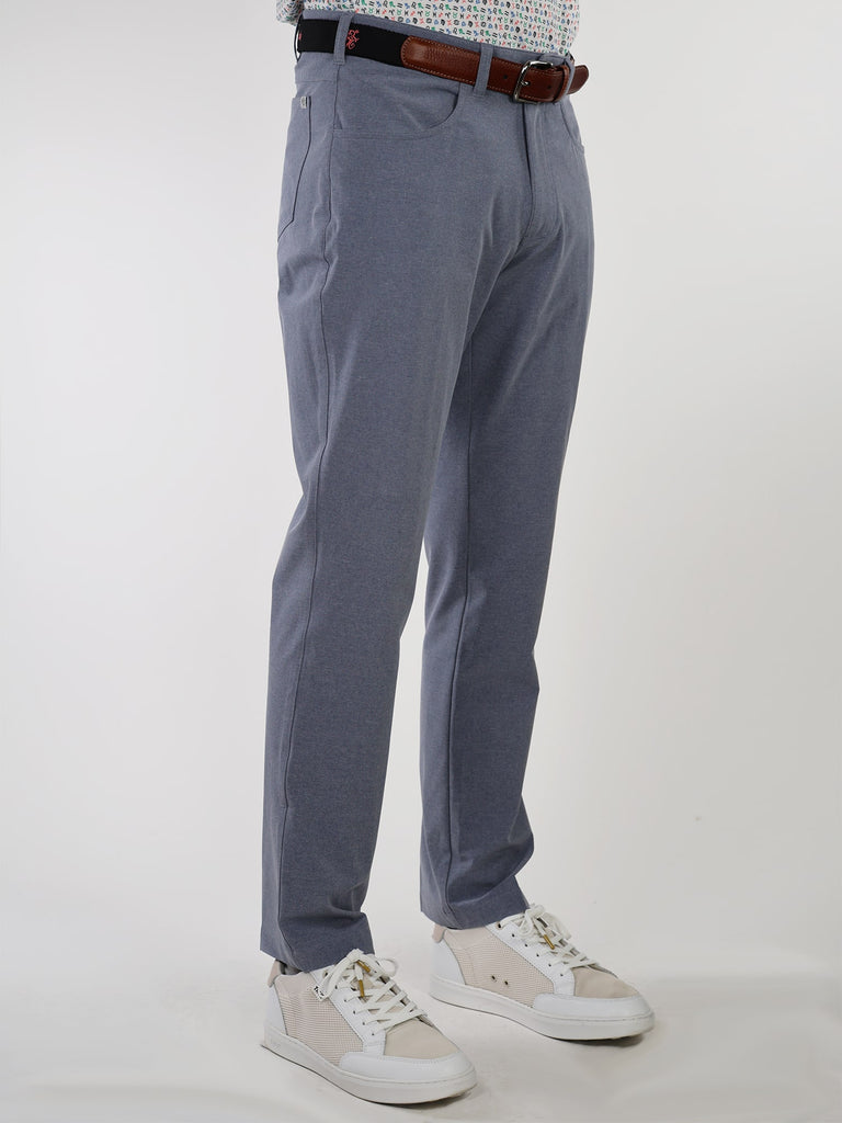 Man wearing slim-fit golf performance pants, white sneakers, and a patterned shirt with a brown belt. The attire is neat and stylish against a plain background.