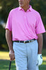 A golfer in a pink polo shirt and beige shorts stands with a golf club in his right hand, preparing to take a shot.