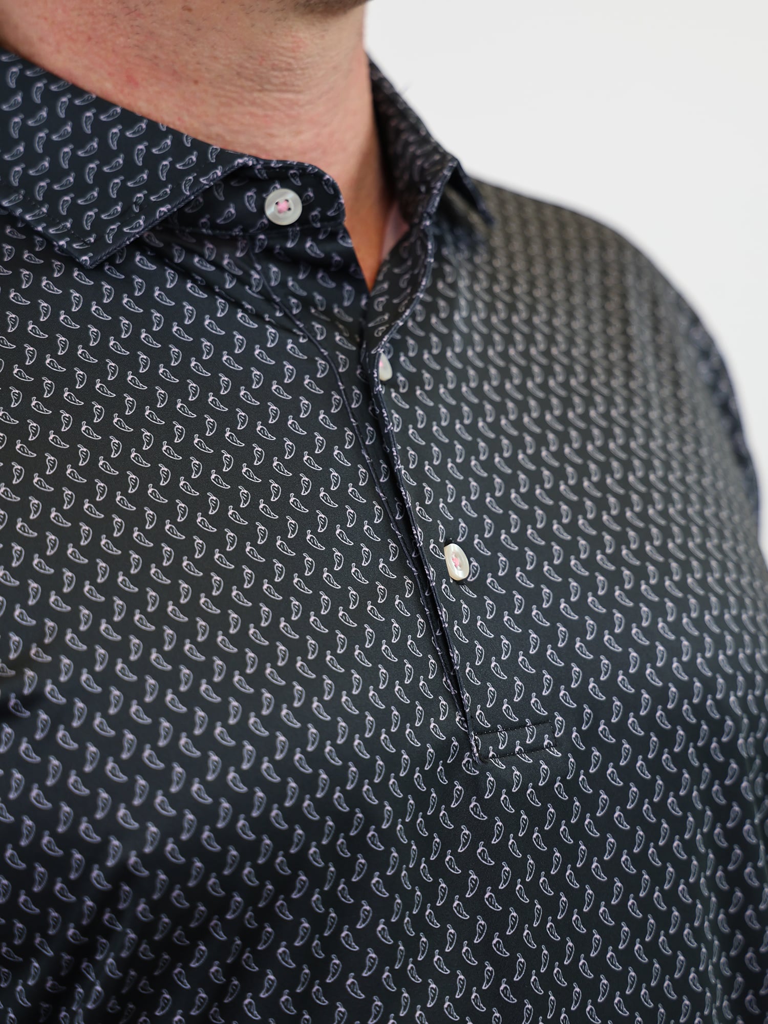 Close-up of a person wearing a black shirt with a small white pepper pattern. The shirt is buttoned, conveying a neat and casual look.