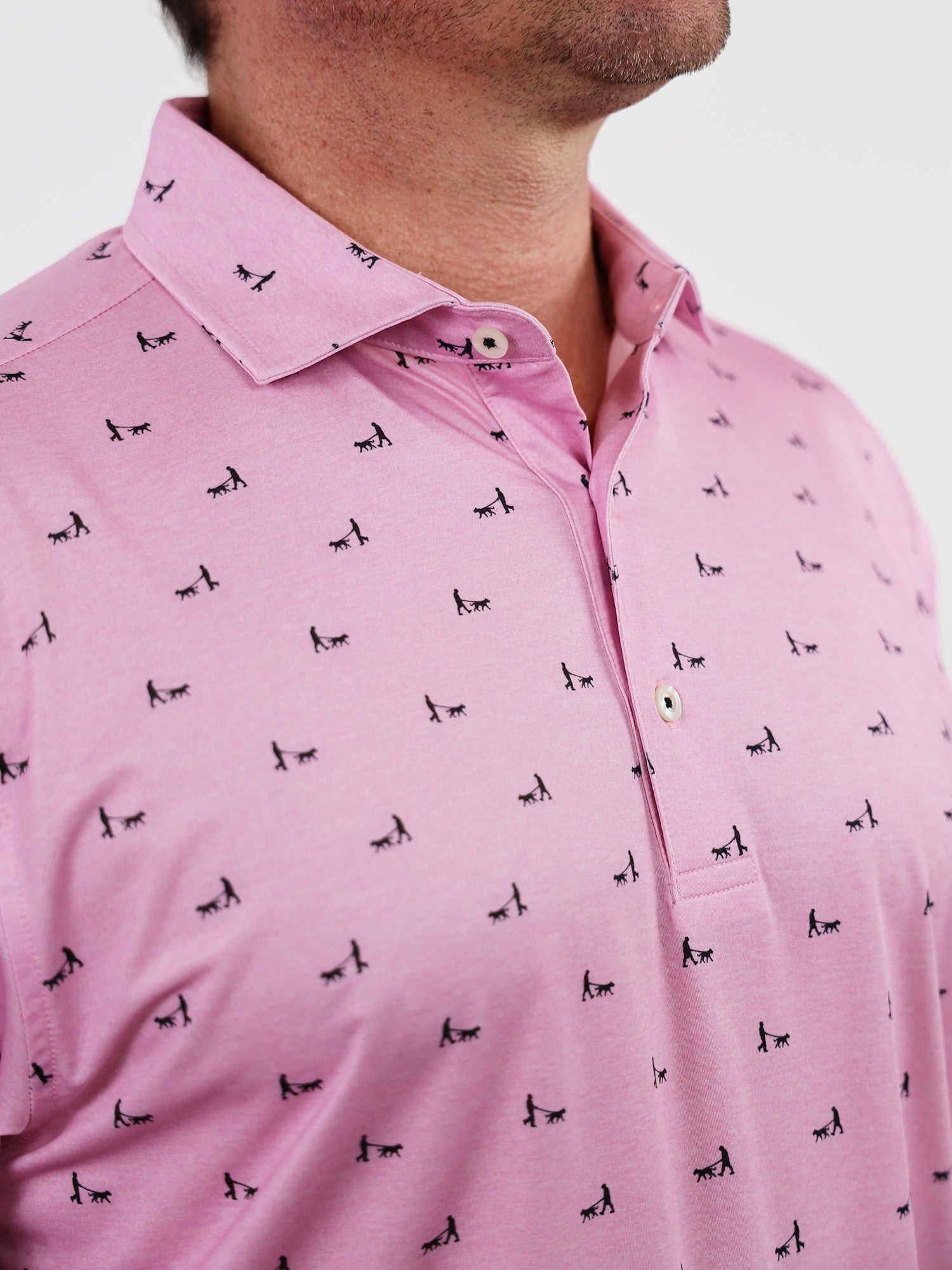 Man wearing a pink collared polo shirt with small, black embroidered dog patterns. The shirt is buttoned, conveying a casual and stylish look