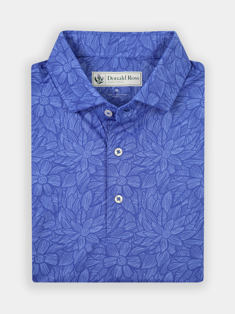 Blue floral-patterned polo shirt, folded neatly. The design features intricate flower motifs. The shirt has a classic collar and white buttons, conveying elegance.