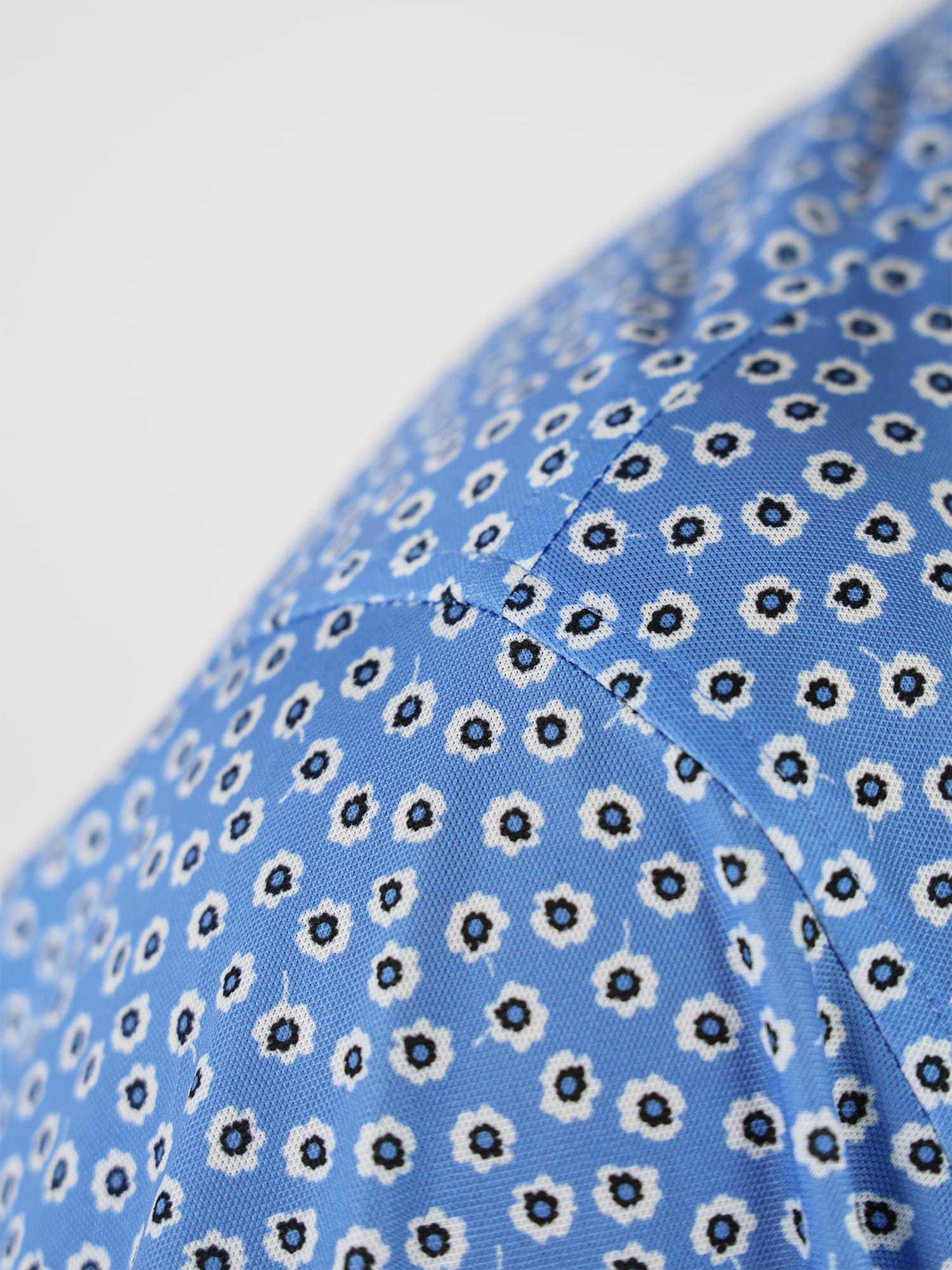 Close-up of the sleeve of a blue golf polo with a pattern of small white and black flowers, creating a playful and vibrant texture.