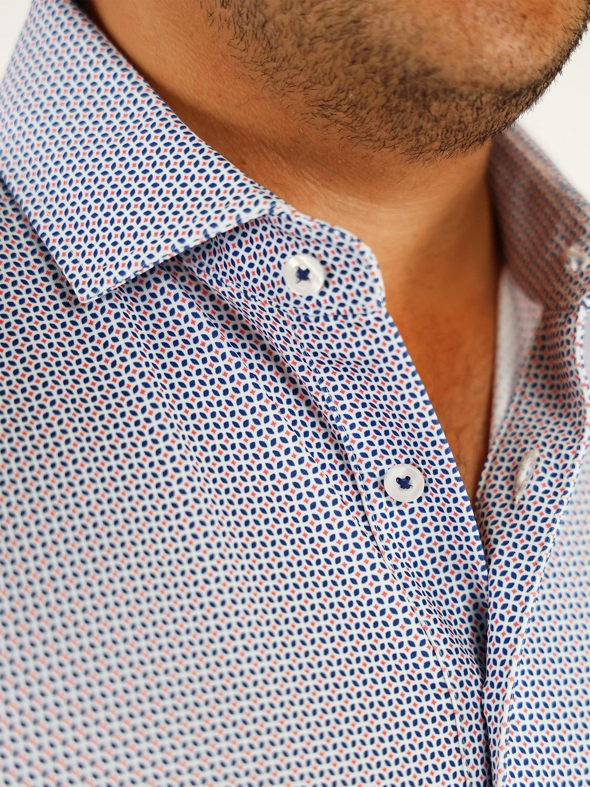 Close-up of a man wearing a patterned button-up shirt with small blue and red geometric designs