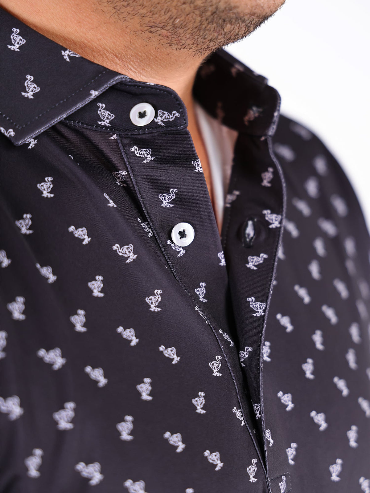 Close-up of a black shirt with white dodo bird pattern. The collar and buttons are visible, creating a casual and stylish feel.