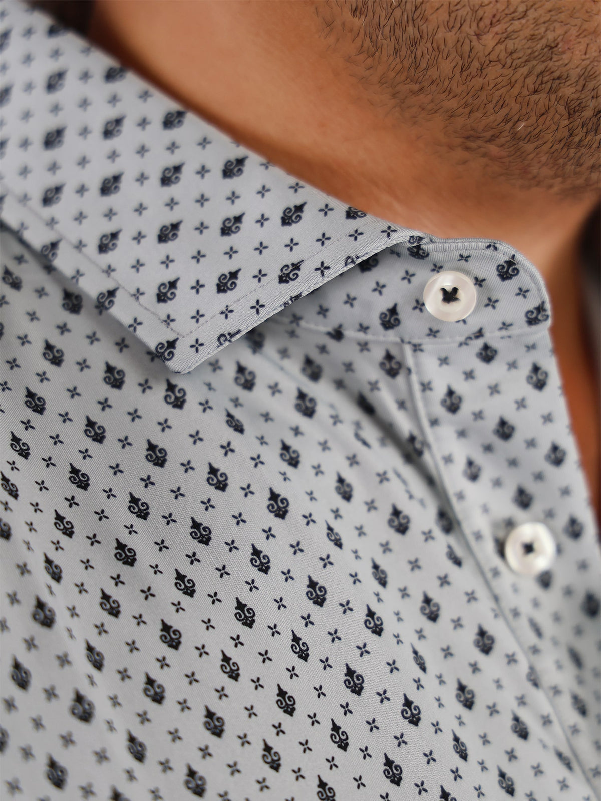 Close-up of a light blue shirt with a small black Donald Ross print pattern. The shirt has silver buttons and a neatly folded collar, conveying a polished look.