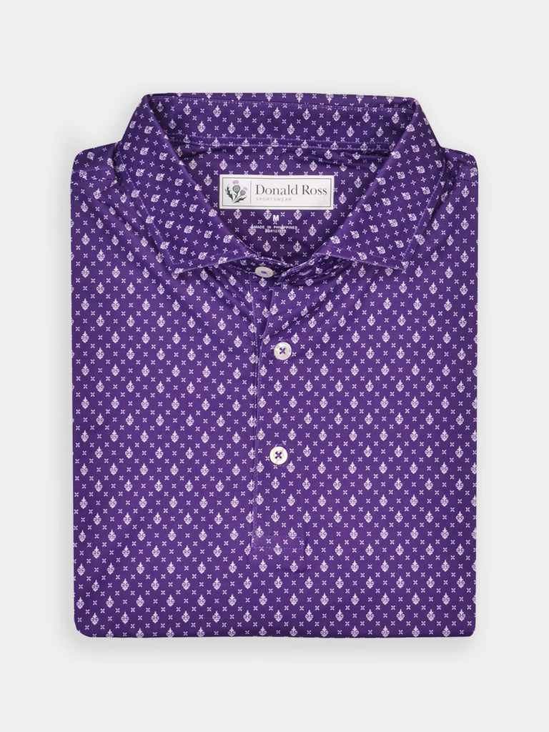 Folded purple polo shirt with a small white royalty pattern, featuring a label at the collar. The shirt's neat folds convey a sense of elegance and style.