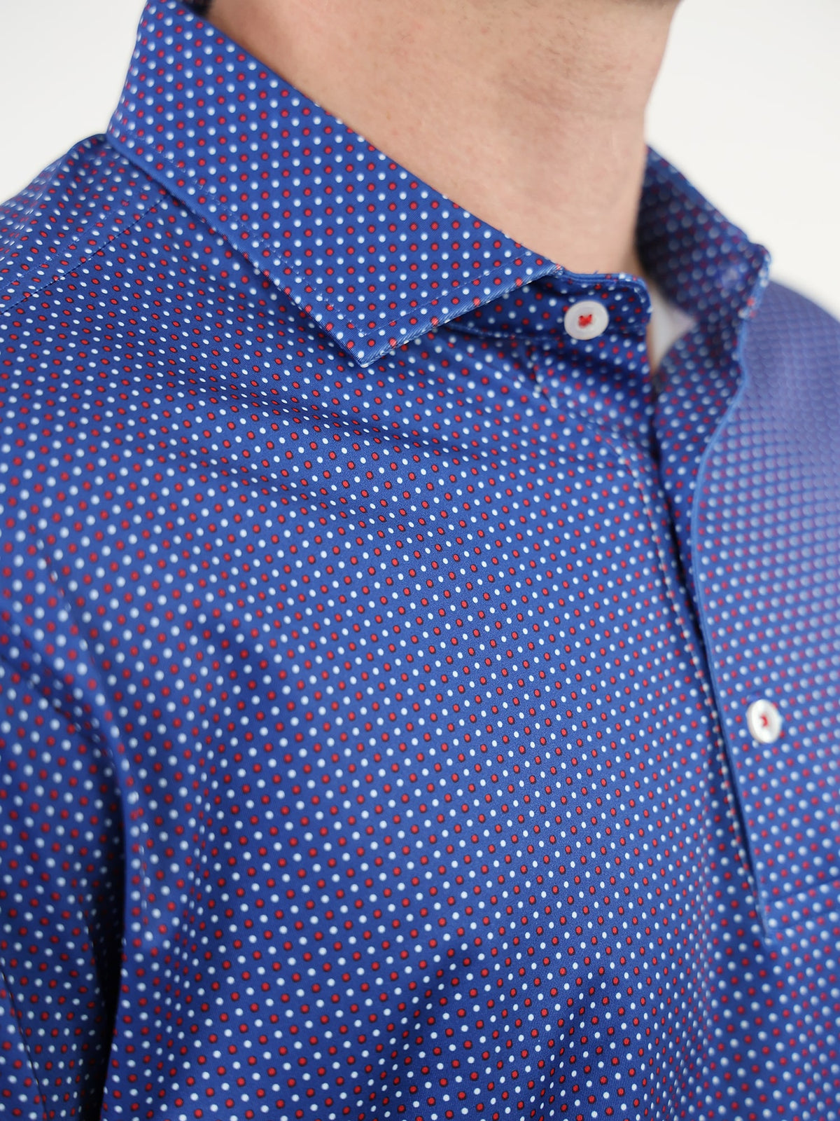 Close-up of a blue dress shirt with a red and white polka dot pattern. The collar is neatly folded, conveying a formal and stylish tone.