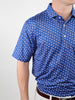 A person wearing a blue golf shirt with a pattern of small Uncle Sam hats. The shirt is tucked into white pants with a brown belt.