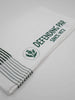 A neatly folded white towel features bold green text reading "Defending Par Since 1872" on a stripe, with a thistle emblem