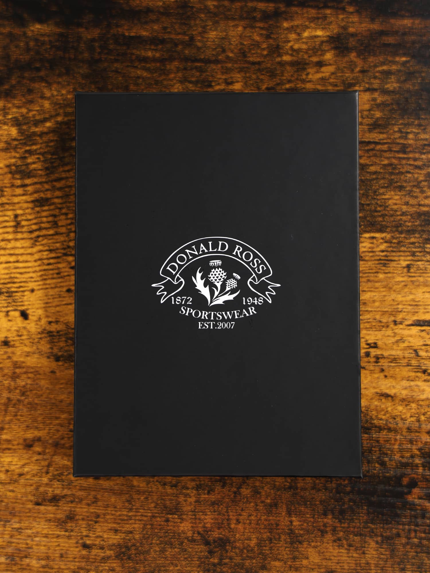 A black box with "Donald Ross Sportswear" logo in white, featuring a thistle design
