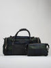 Black leather duffel bag set with green zippers, placed on a neutral backdrop