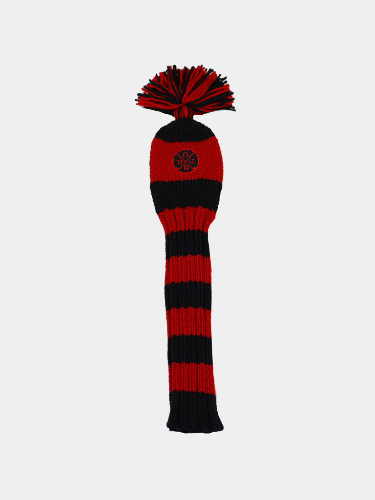 Red and black striped knitted golf club cover with a pom-pom at the top and an emblem featuring crossed golf clubs. The cover conveys a sporty and classic tone.