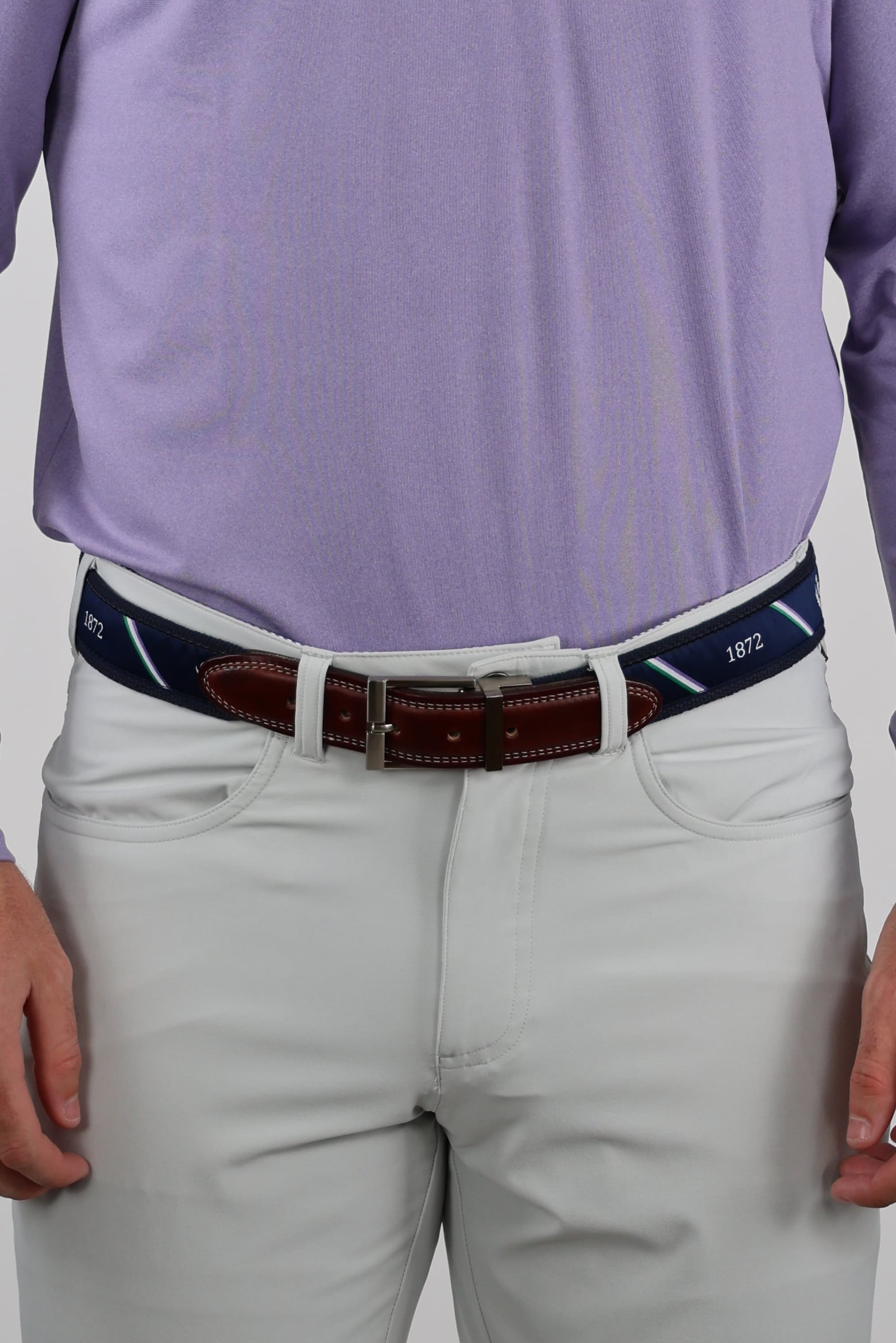 Man wearing a light purple shirt tucked into white pants with a navy and brown belt. The belt features the numbers "1872" and has a silver buckle.