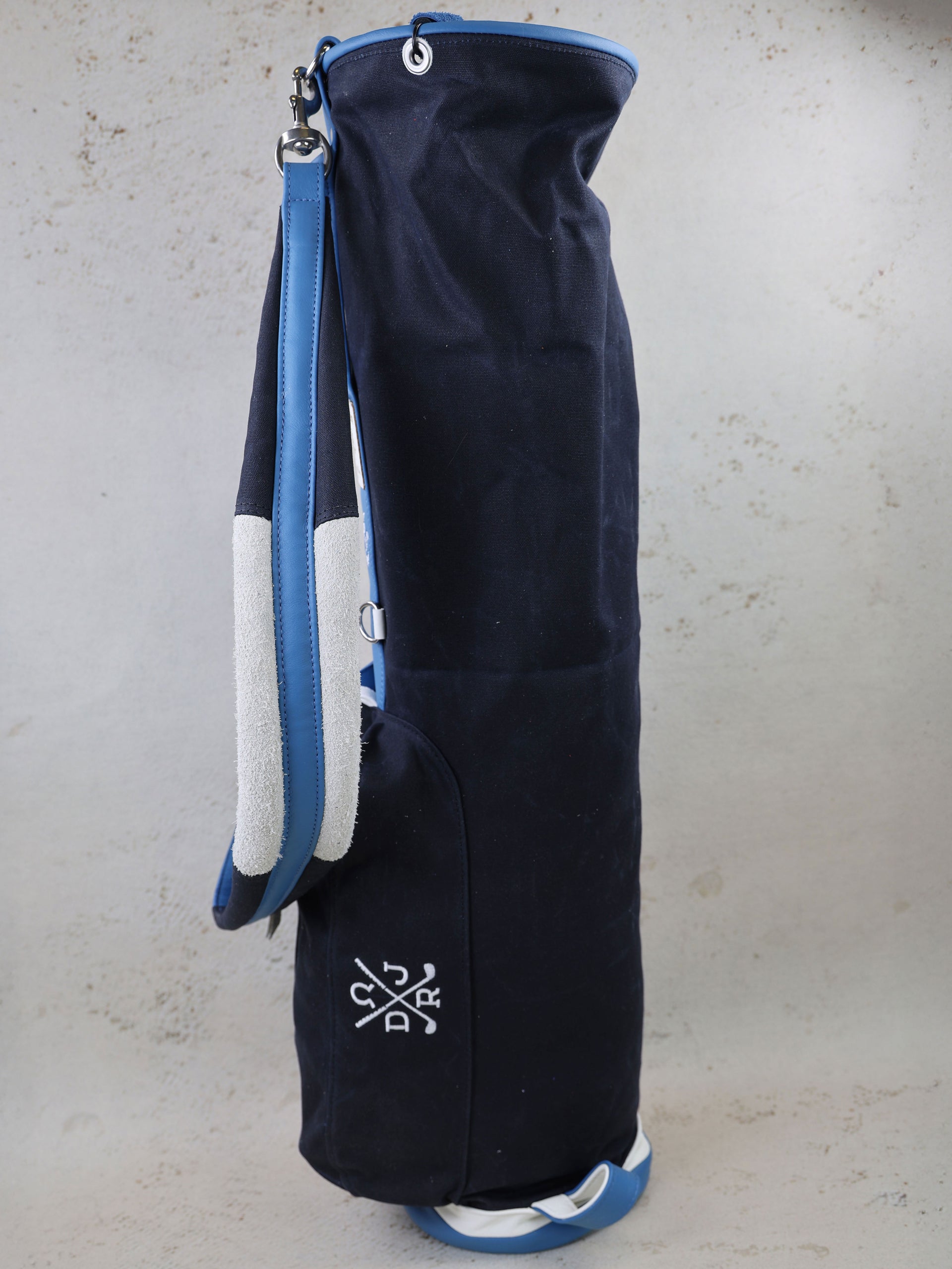 Navy canvas golf bag with blue leather handles, white trim accents, and embroidered crest logo displayed against a neutral background.