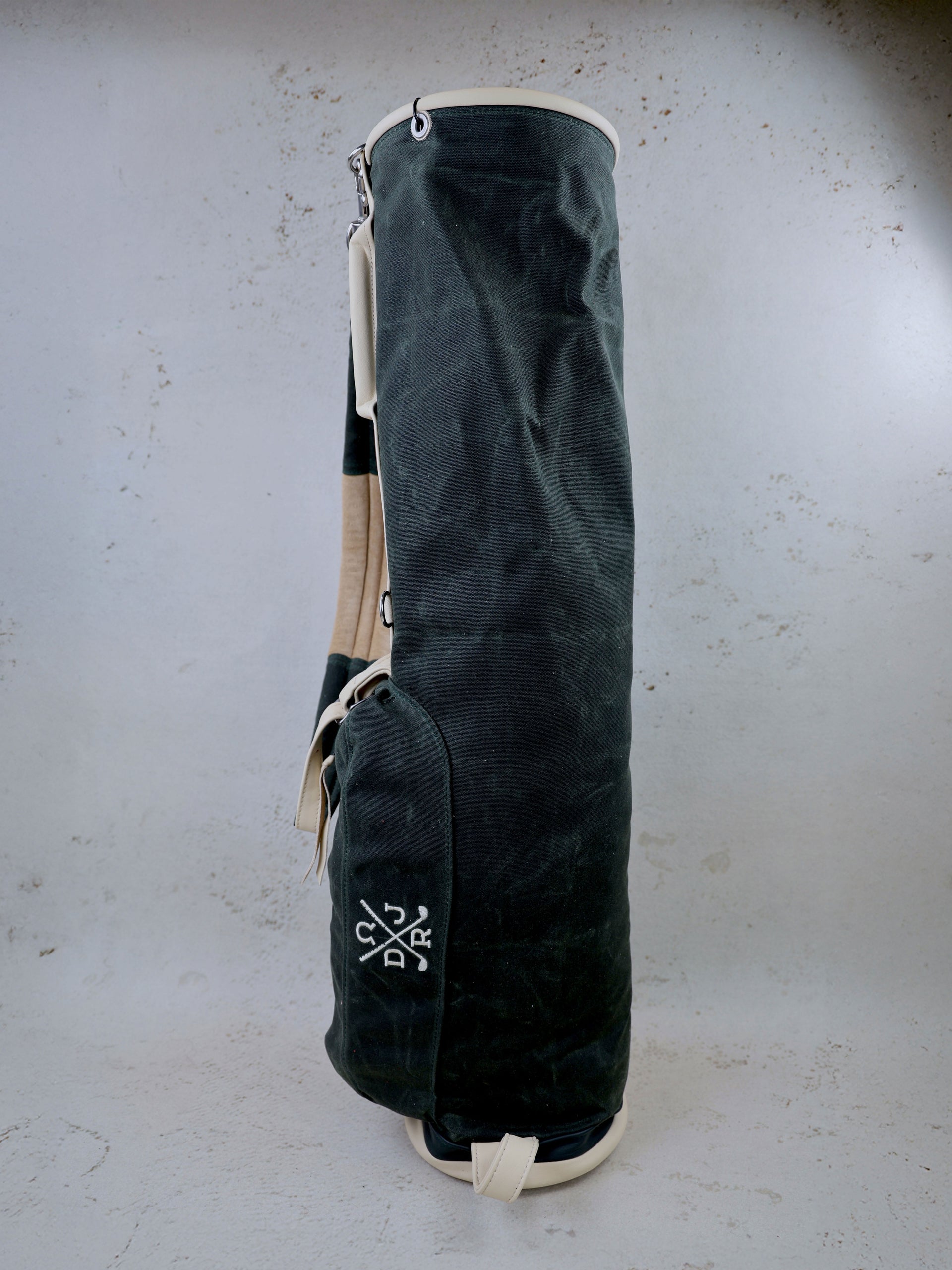 Dark canvas golf bag with cream-colored trim and handles displayed upright against a neutral background.