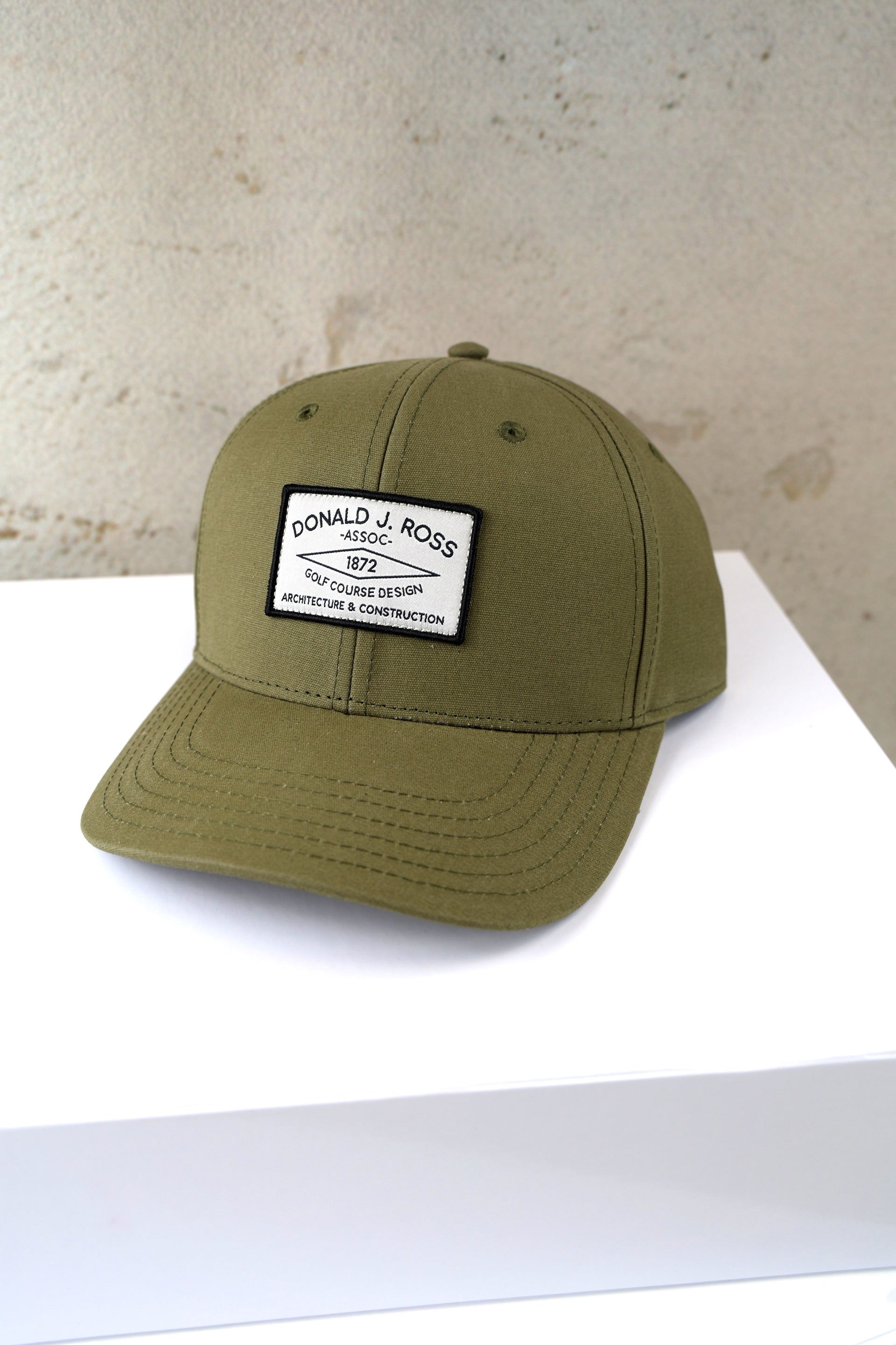 Olive green baseball cap with white woven patch reading "Donald J. Ross Assoc. 1872 Golf Course Design Architecture & Construction."