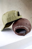 Two adjustable caps displaying embroidered text, one in sage green and one in brown, arranged on a white surface.