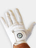 A white golf glove with perforations displays a circular logo on the wrist and is held by a hand against a neutral background.