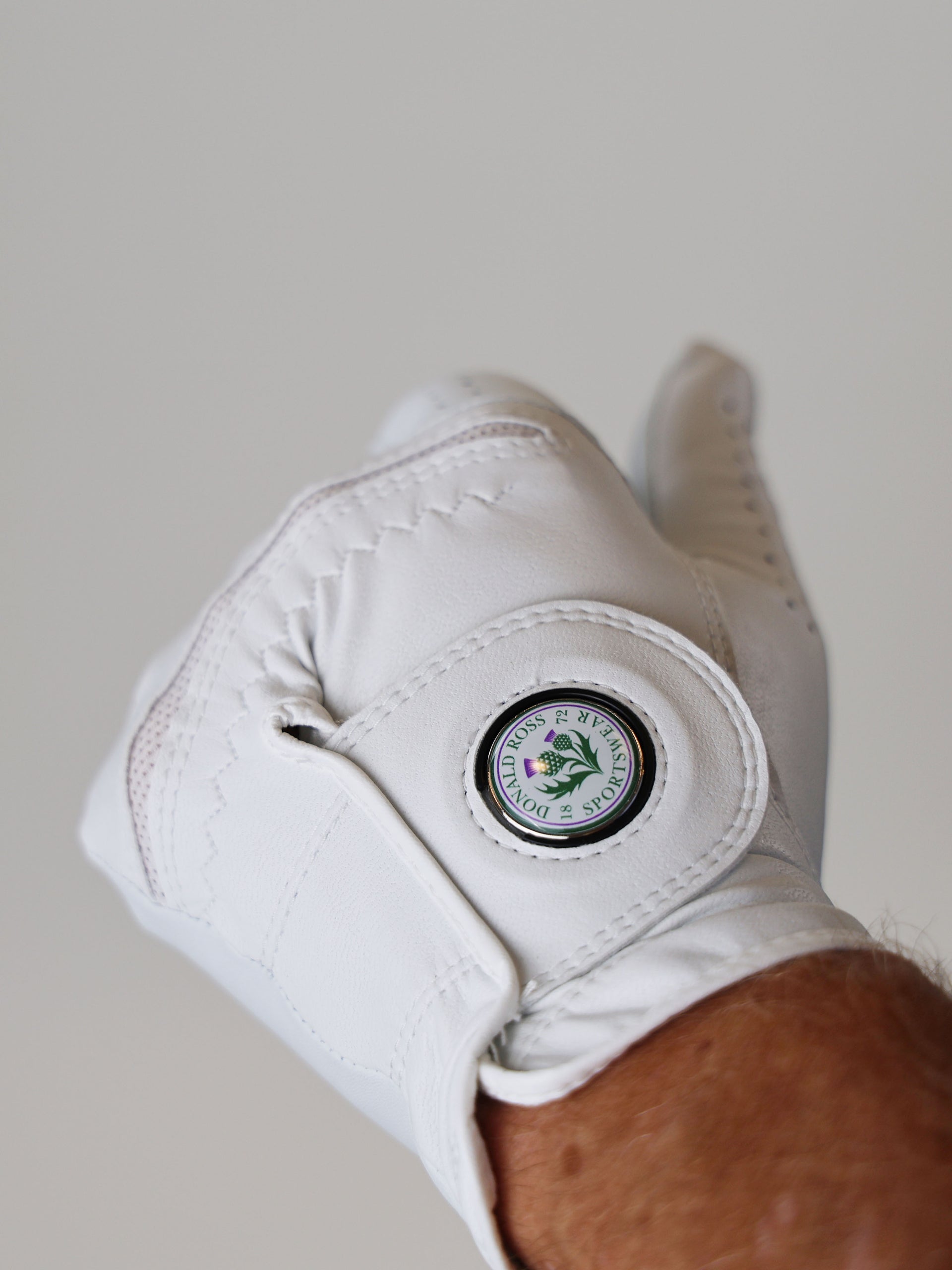 A white golf glove is displayed with a round emblem on the wrist area, shown against a plain background.