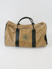 Tan duffel bag with dark handles and a round green emblem featuring floral design. The bag rests on a plain white surface, offering a vintage feel.