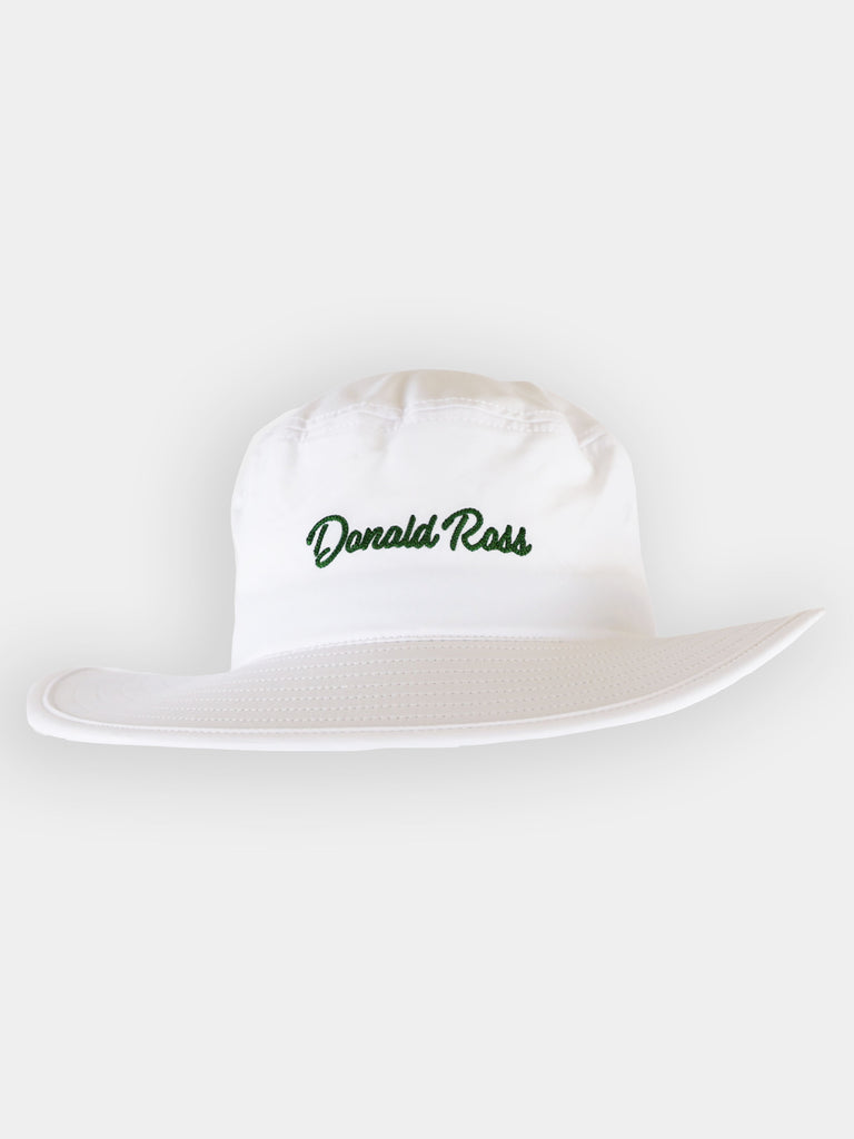A white bucket hat with a floppy 2 1/4 inch brim and the name Donald Ross embroidered in navy blue script on the front crown.