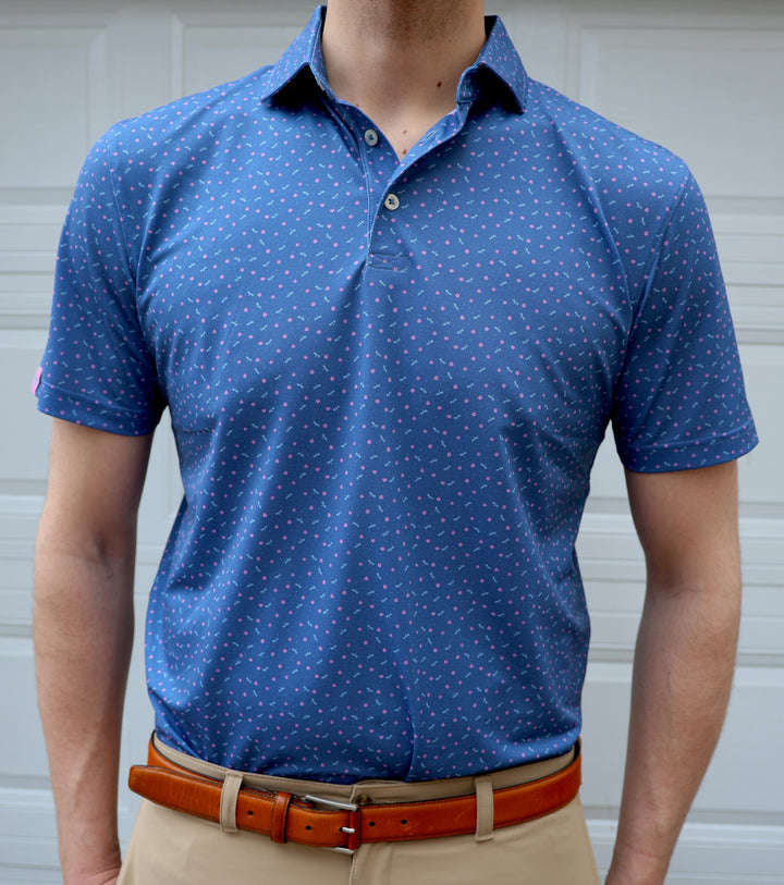 A person is wearing a blue polo shirt with a pattern of small pink shapes and khaki pants, standing in front of a garage door.